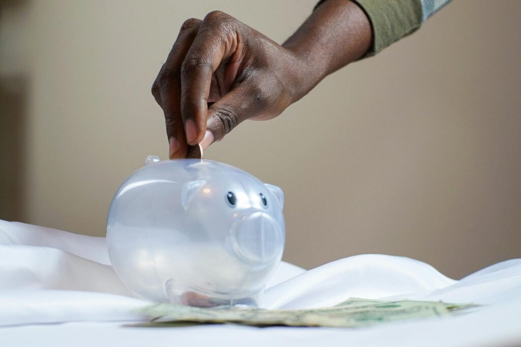 A person placing coins into a labeled emergency fund jar on a table with budget documents and a calculator beside it